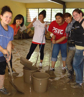 Group of young women cleaning up the mud in a room that has been flooded.