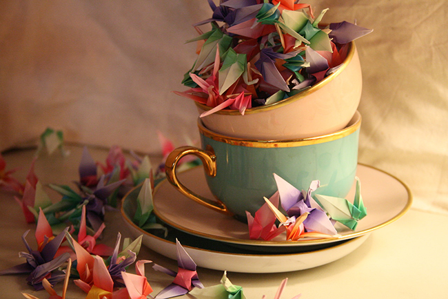 Two cups on two saucers filled with little colourful origami cranes