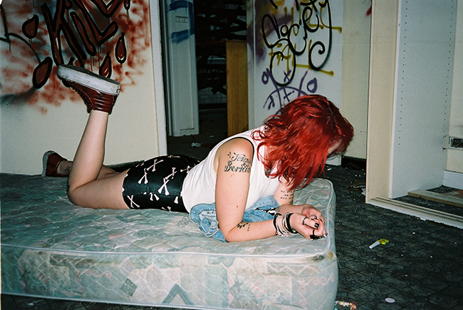 Girl with red hair lying on a mattress in a room with graffiti on the walls