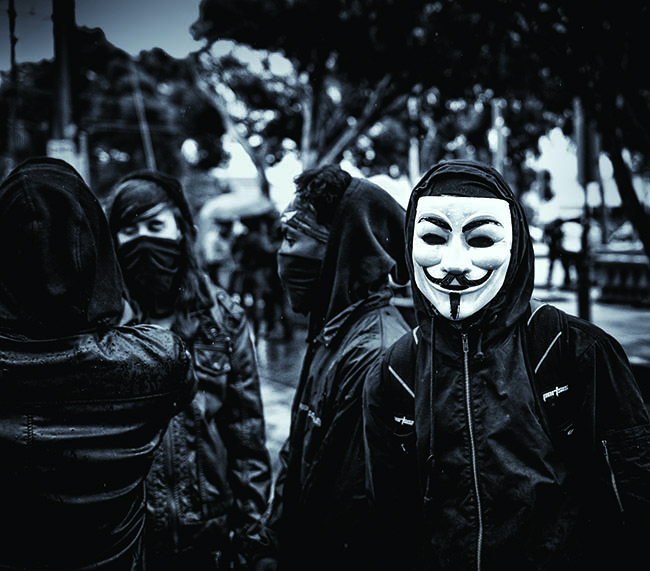 Man in Anonymous mask among three cloth masked people.