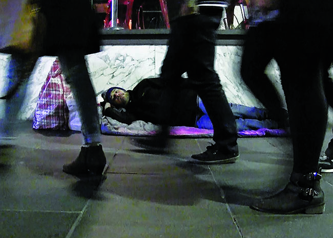 Image of homeless person sleeping on ground and people walking past